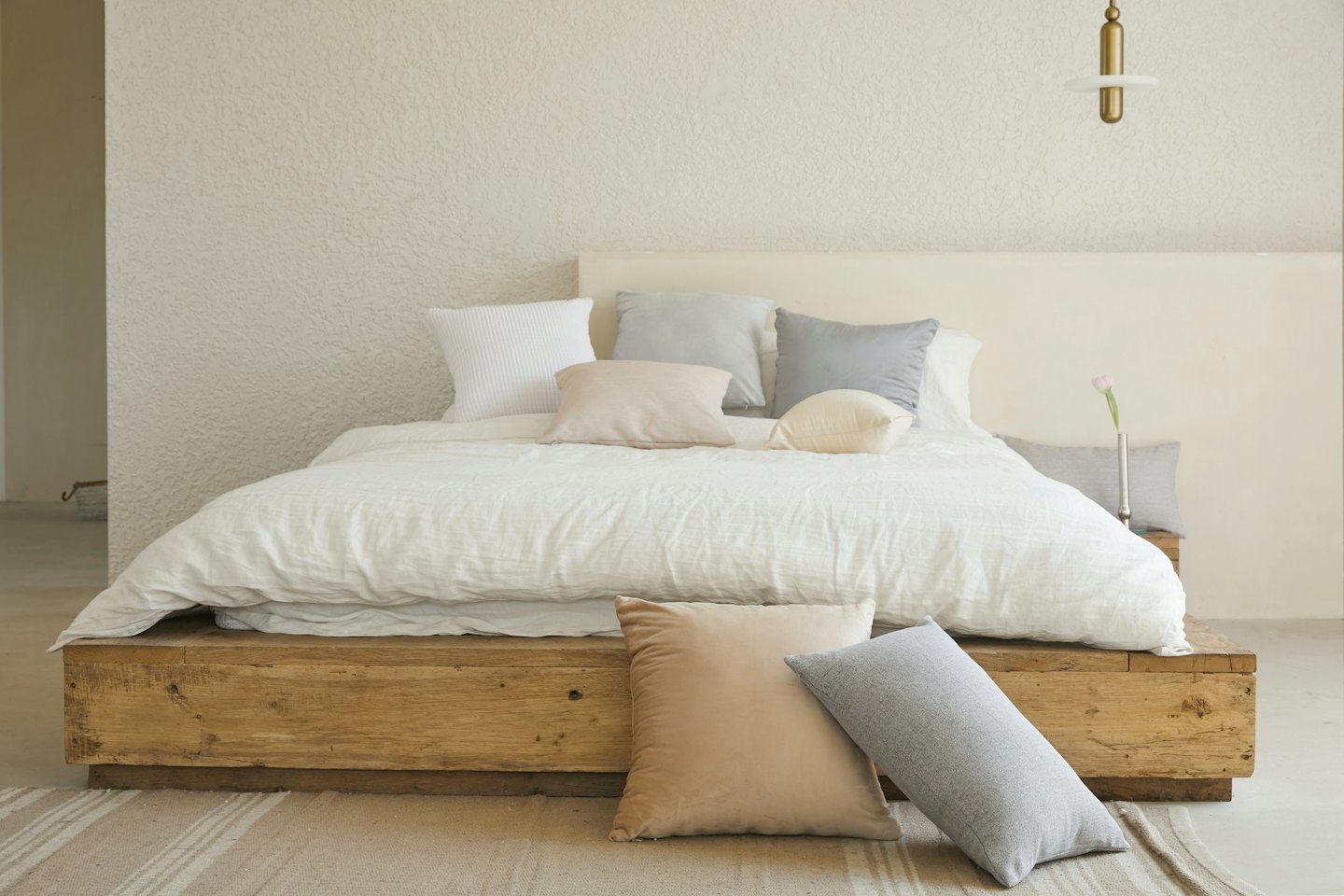 A minimalist bedroom with a large bed, striped rug, and single tulip.