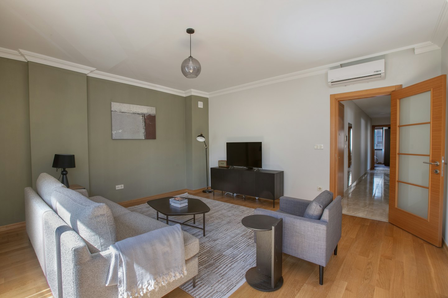 Modern living room with sage green accent wall and grey sofa.