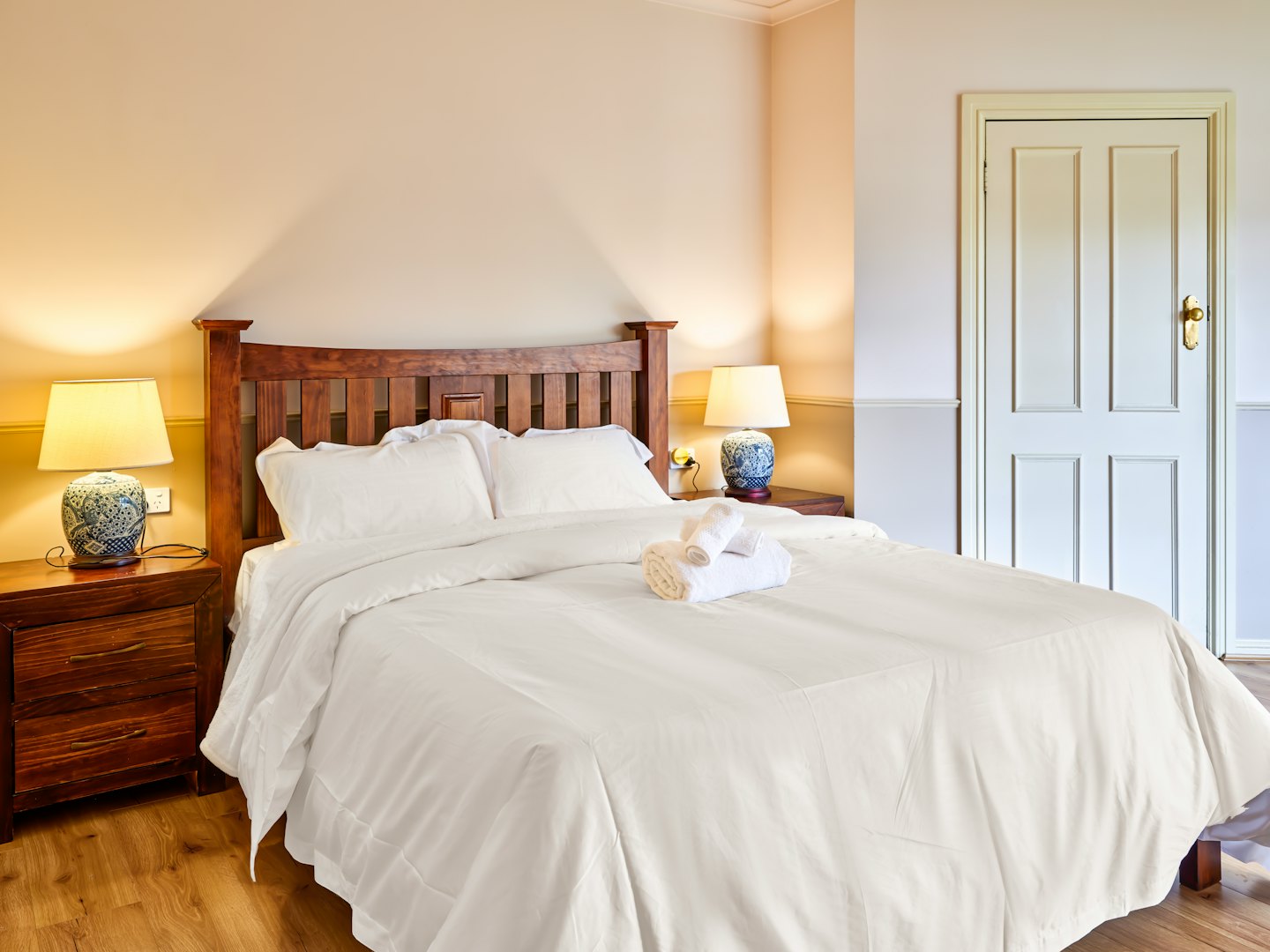 A made bed with a wooden headboard and blue lamps.